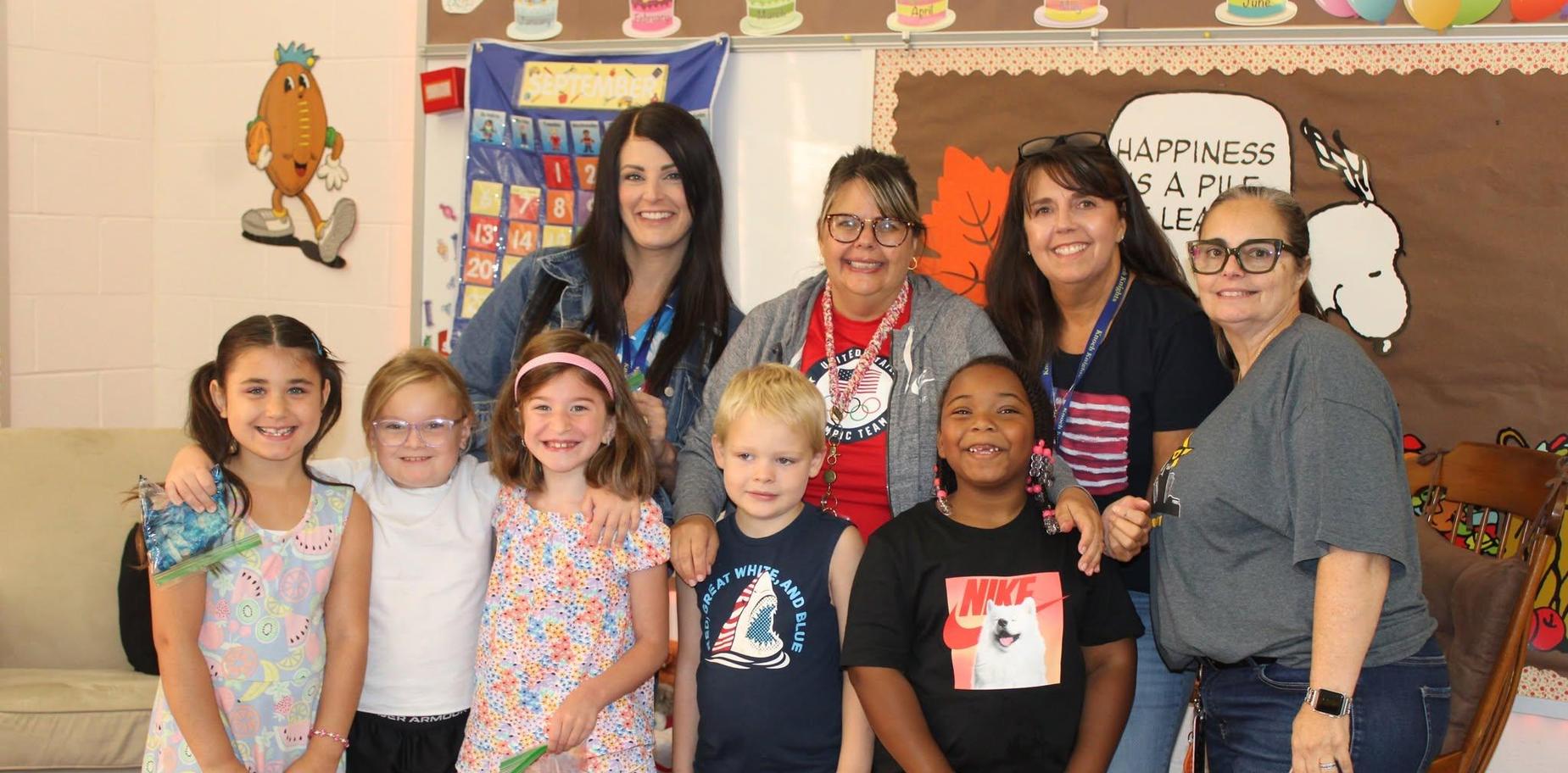 A diverse group of adults and children smile for a group photo in a classroom setting.