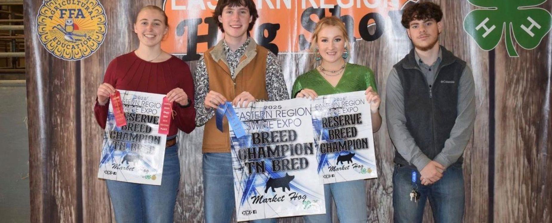 Four individuals proudly display their award posters at an event.