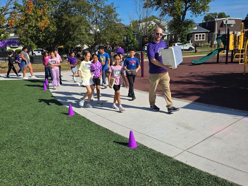 A group of children and an adult walking on a path near a playground during an outdoor event.