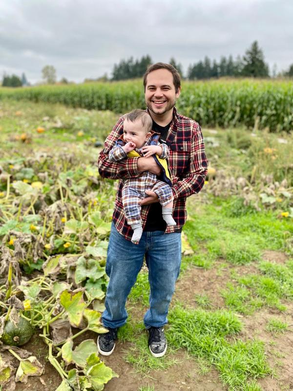 Arco Iris Spanish Immersion School PE teacher David Zahn stands in a pumpkin and corn field holding his son.