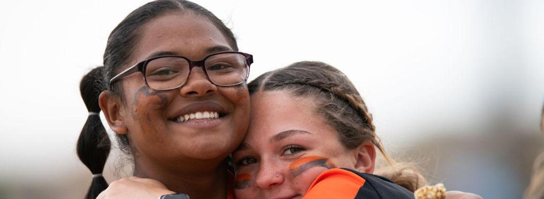 Two smiling young women embracing while wearing sports team gear.