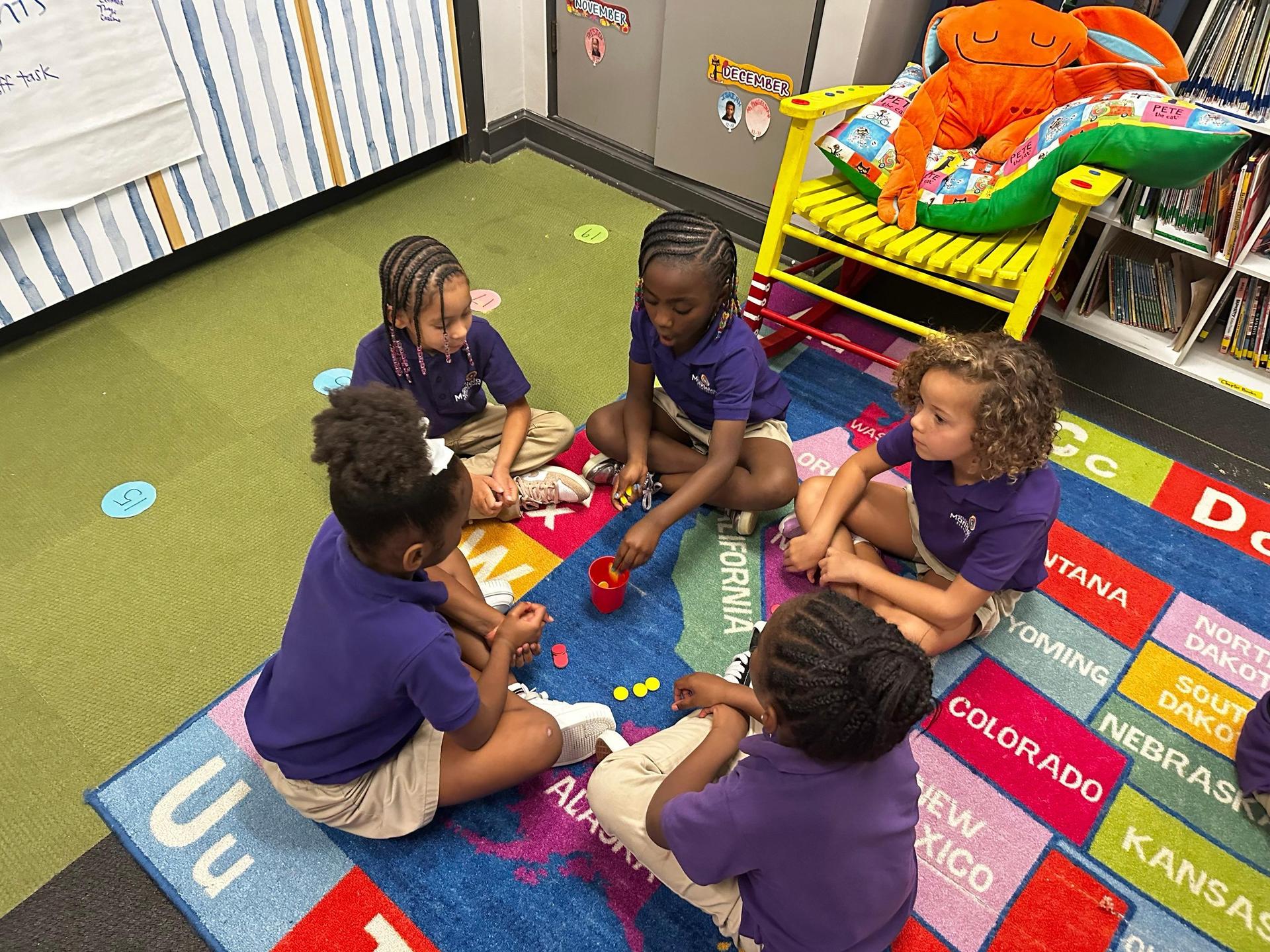 Scholars sit on a colorful rug doing an activity