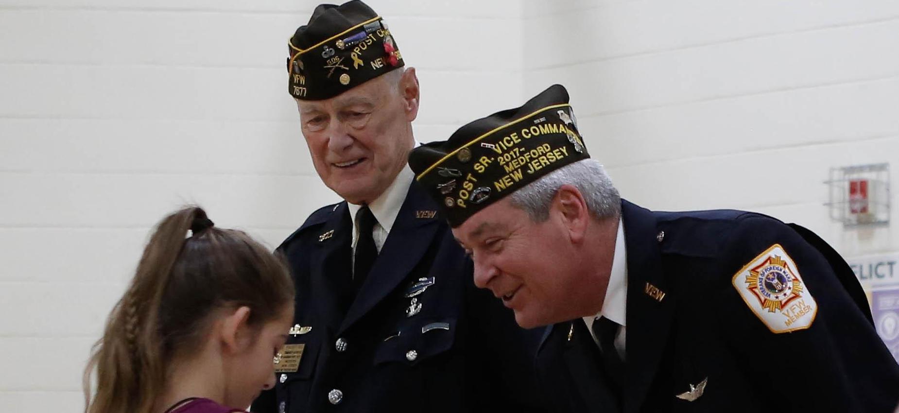 Picture of a student shaking hands with two Veterans during a Veterans Day ceremony 2019