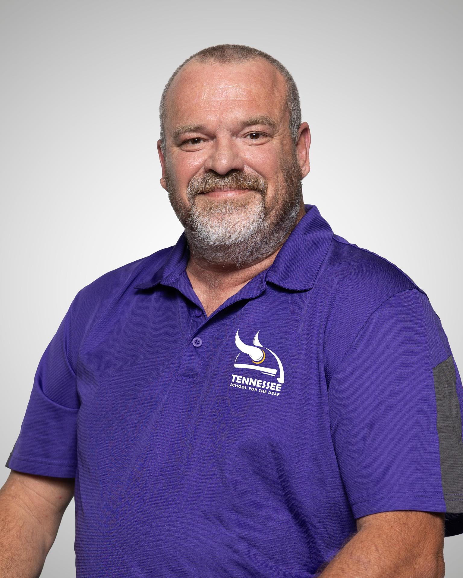 Man with a beard wearing a purple polo shirt with the Tennessee School for the Deaf logo.