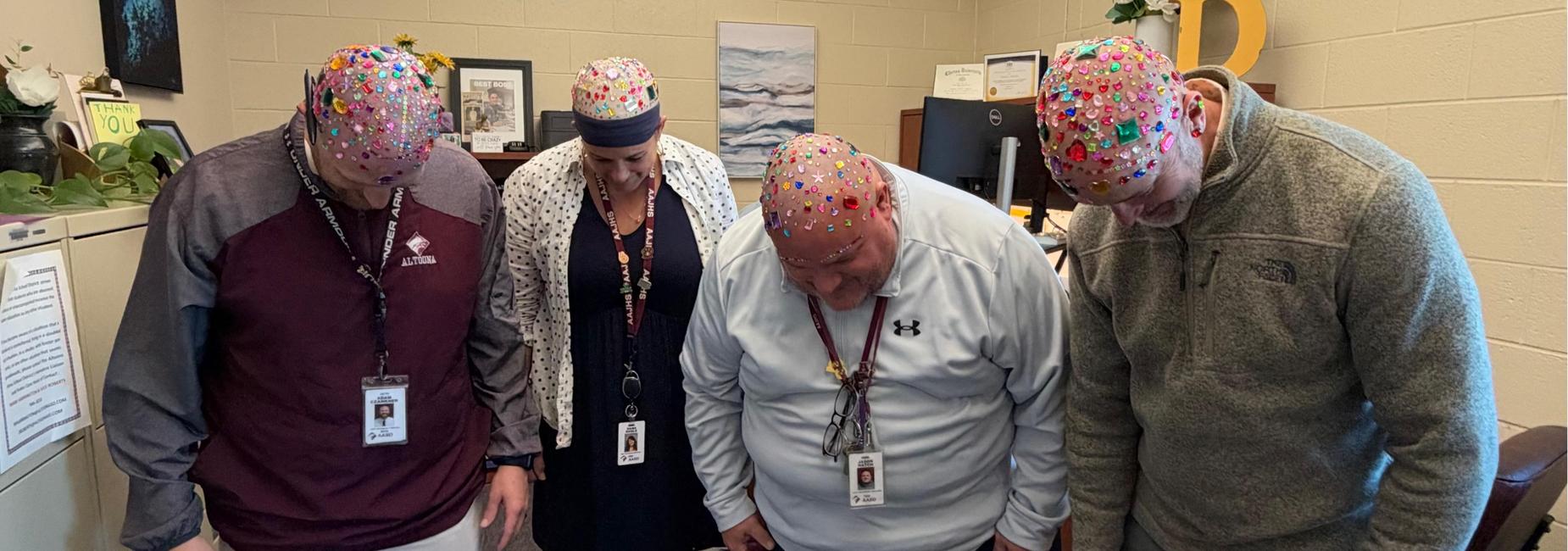 Four people with colorful hats standing together, looking down.