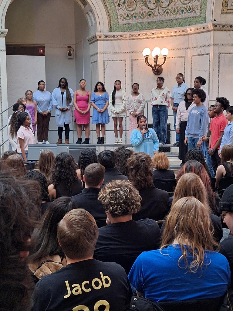 Choir singing in front of seated crowd.