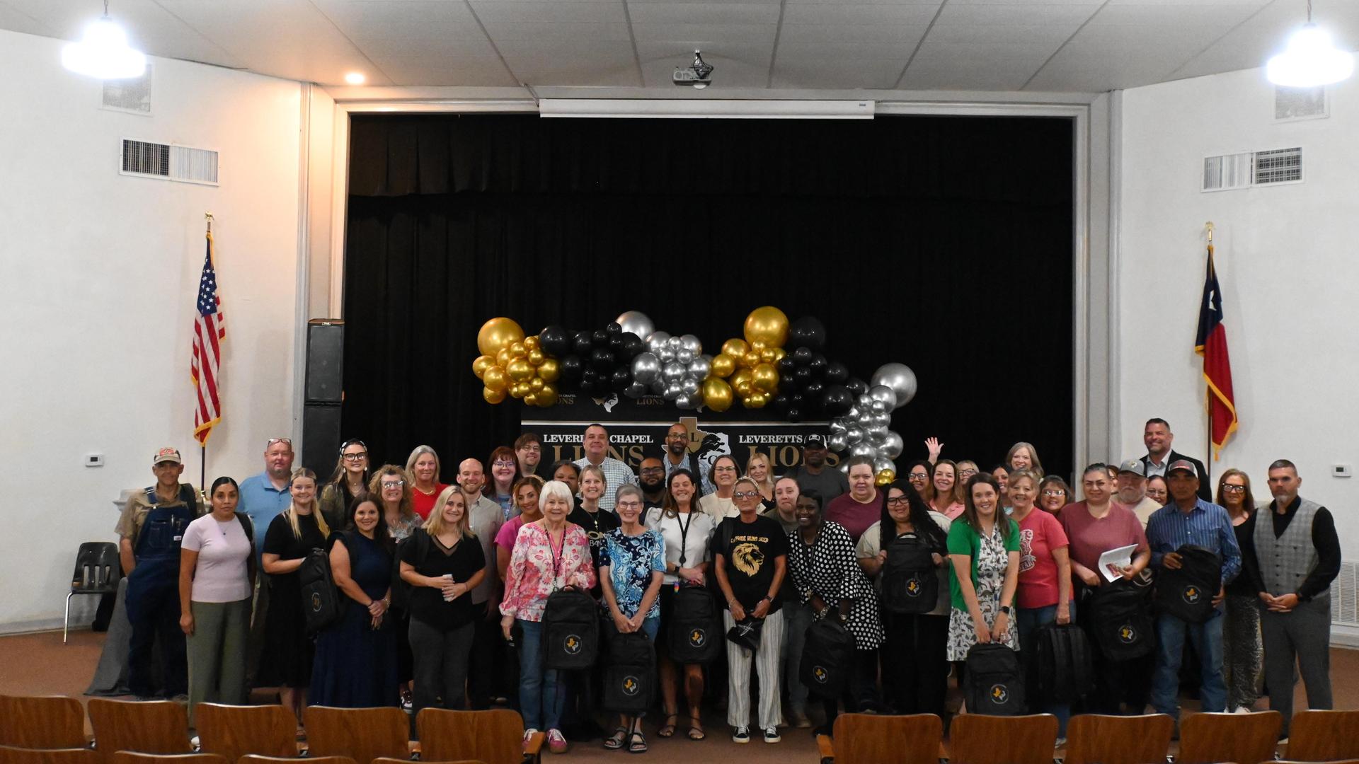 A large group of people posing in an auditorium with balloons and flags.