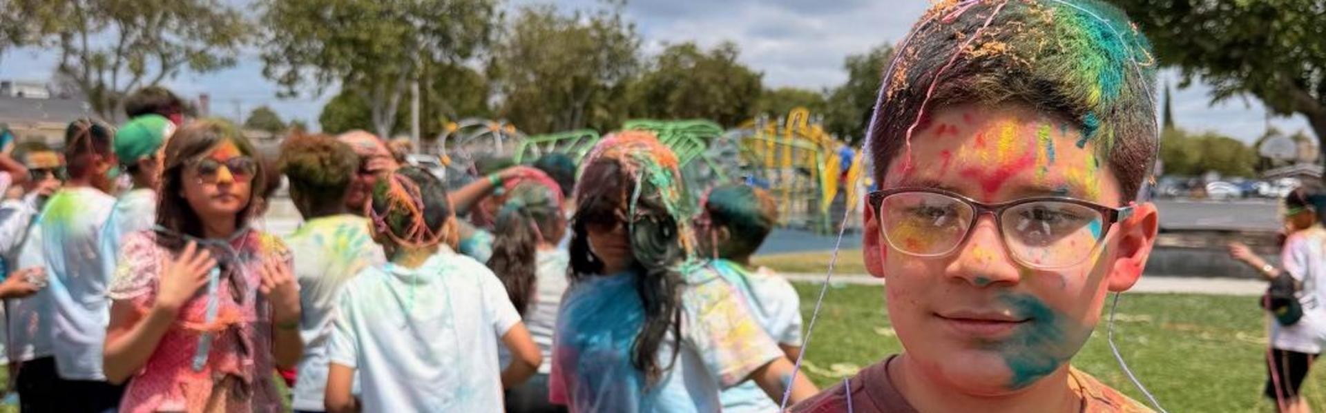 A boy looking at the camera amidst a crowd covered in colorful powder.