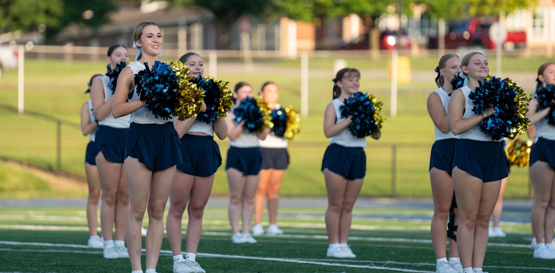 Cheerleaders standing on a field with pom-poms, smiling at the event.