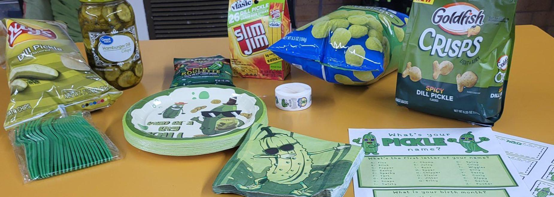 A table set with green utensils, pickle-themed plates, napkins, and a name game sheet.