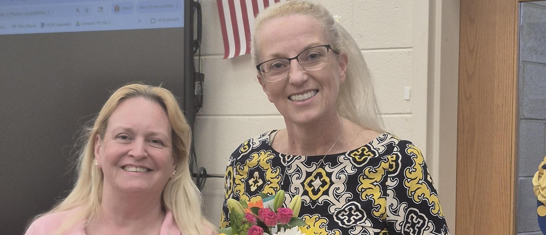 Two women holding a flower bouquet, smiling for the camera.