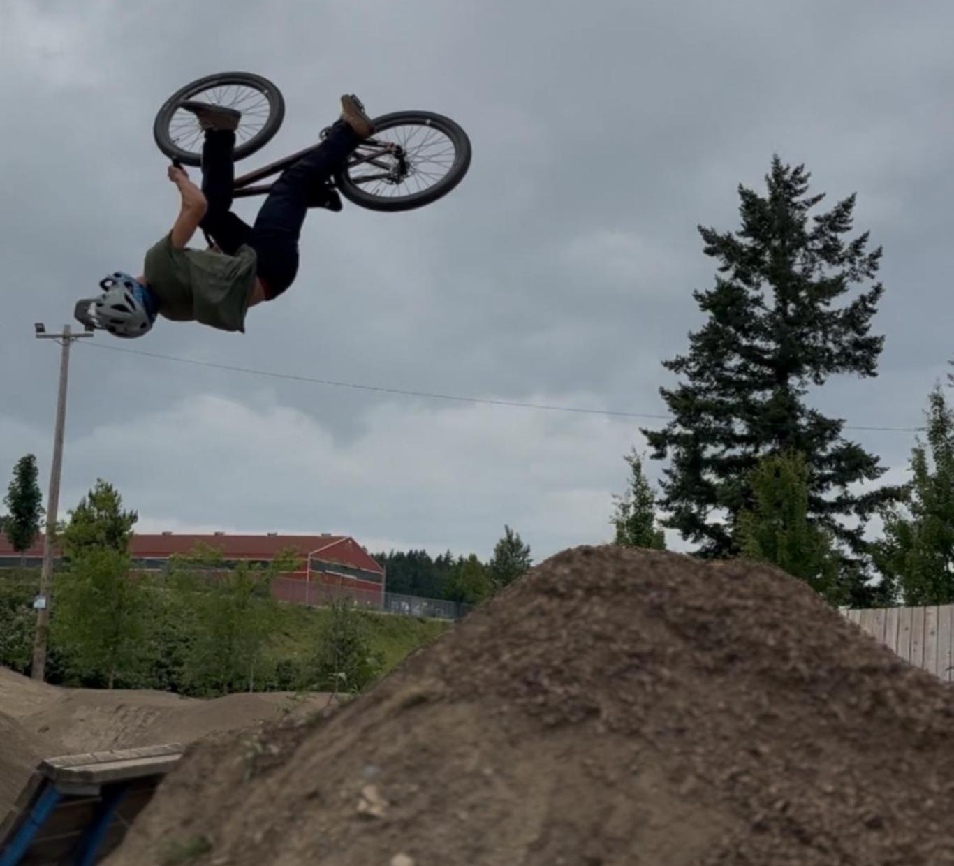 A person performs a bicycle stunt in mid-air over a dirt mound.