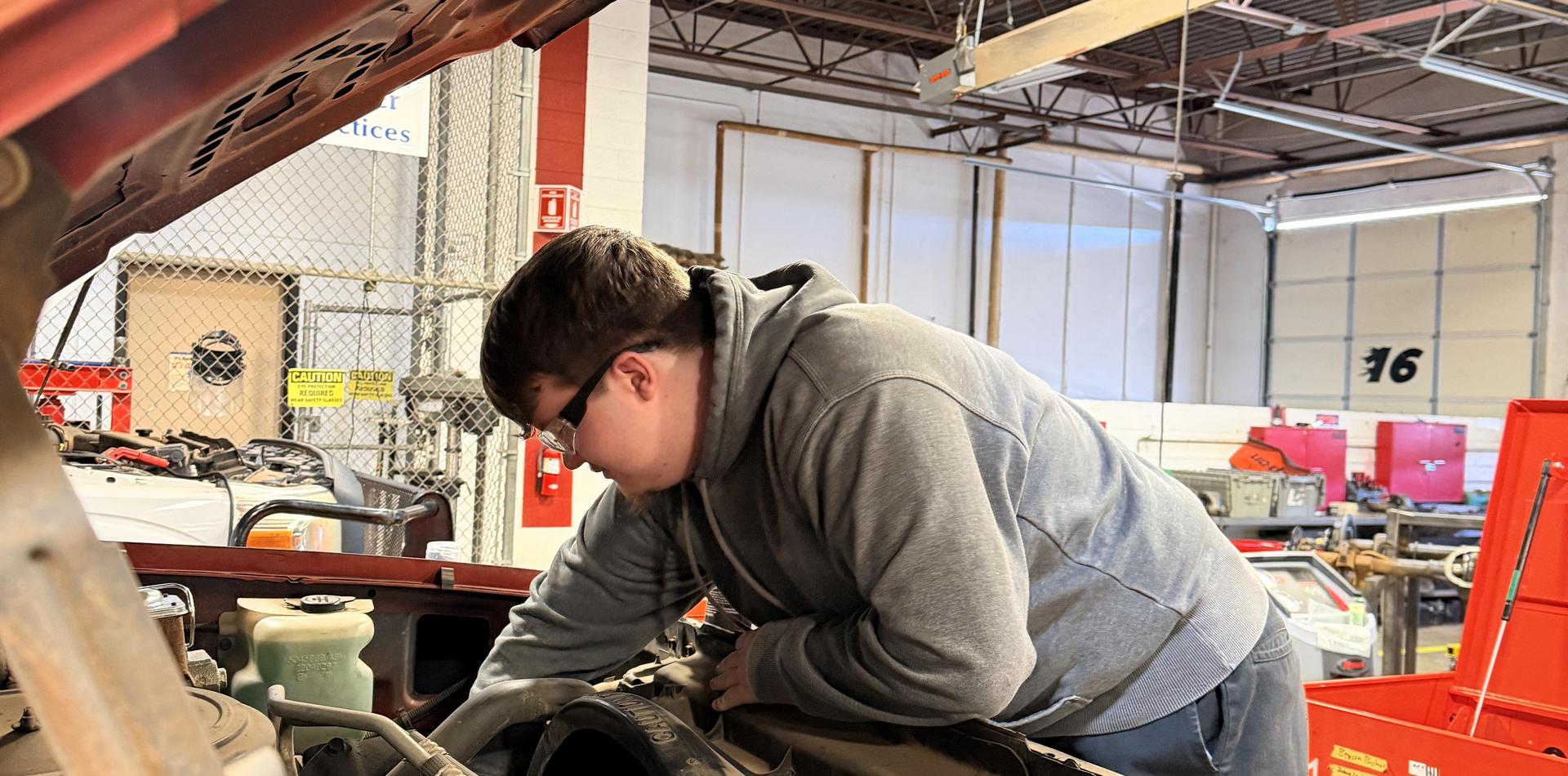 A person working under the hood of a car in a garage setting.