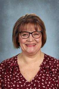 Cheerful woman with short brown hair, wearing glasses and a polka dot blouse.