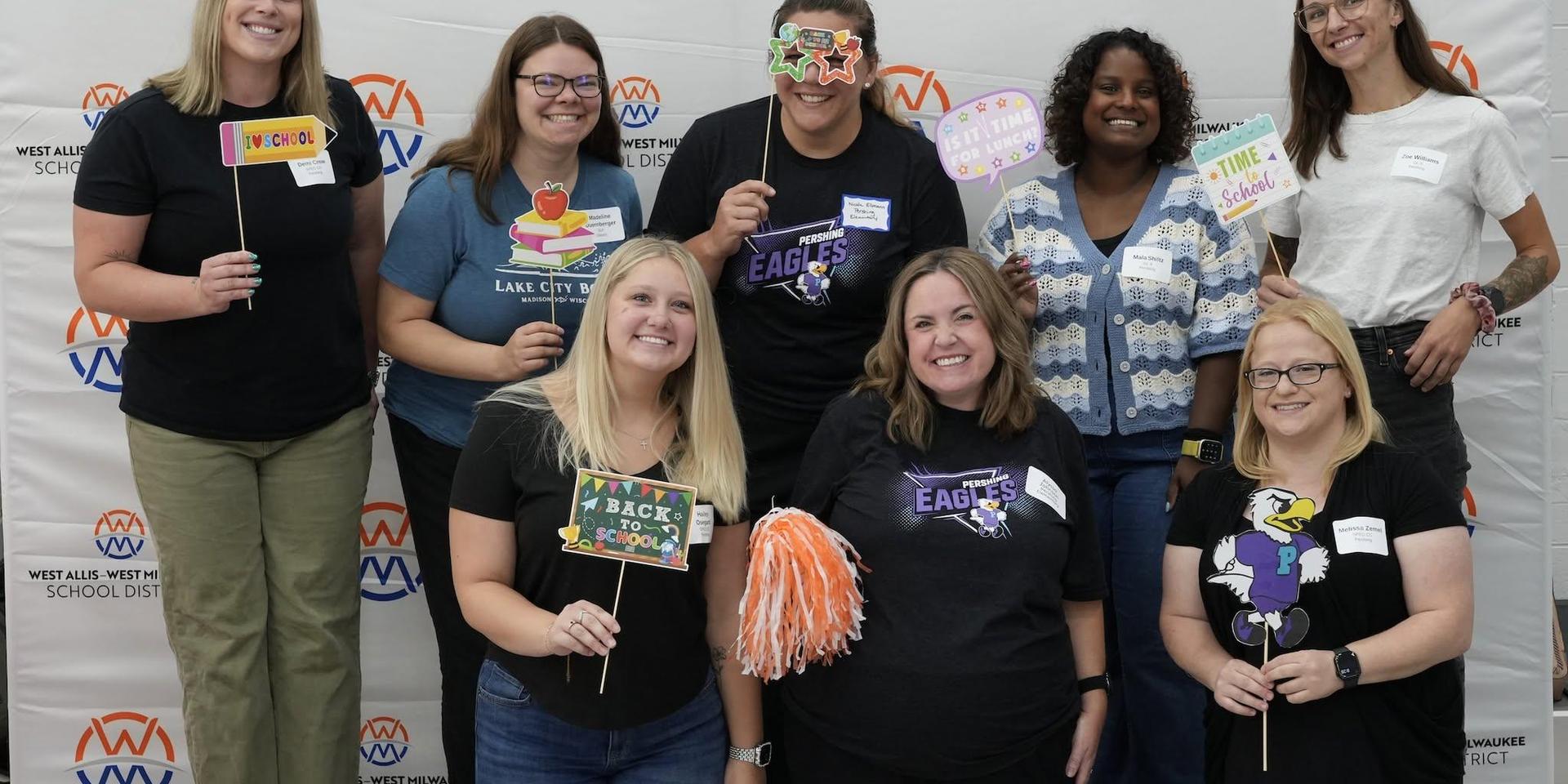 Group of smiling people holding fun signs at a school event.