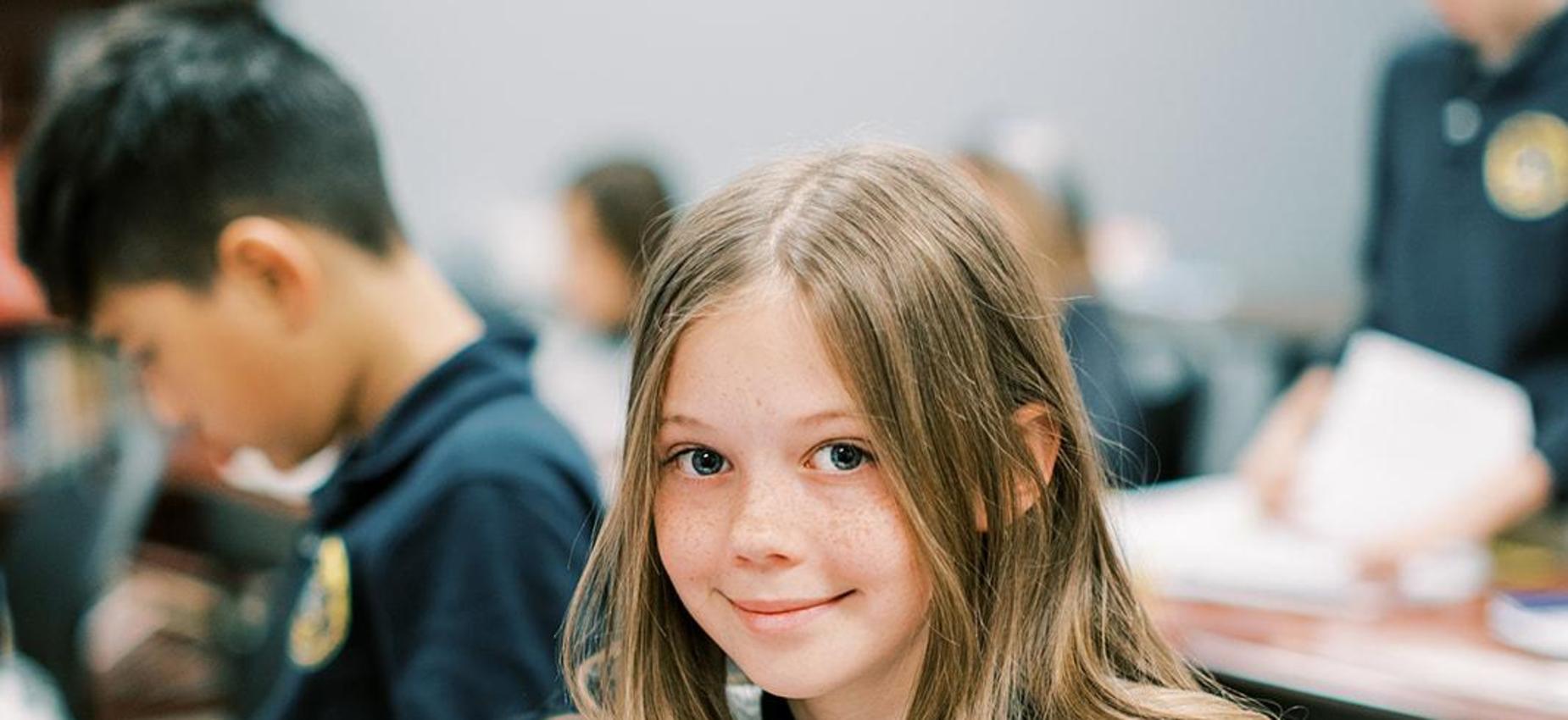 Smiling elementary student looks up from her work at her desk