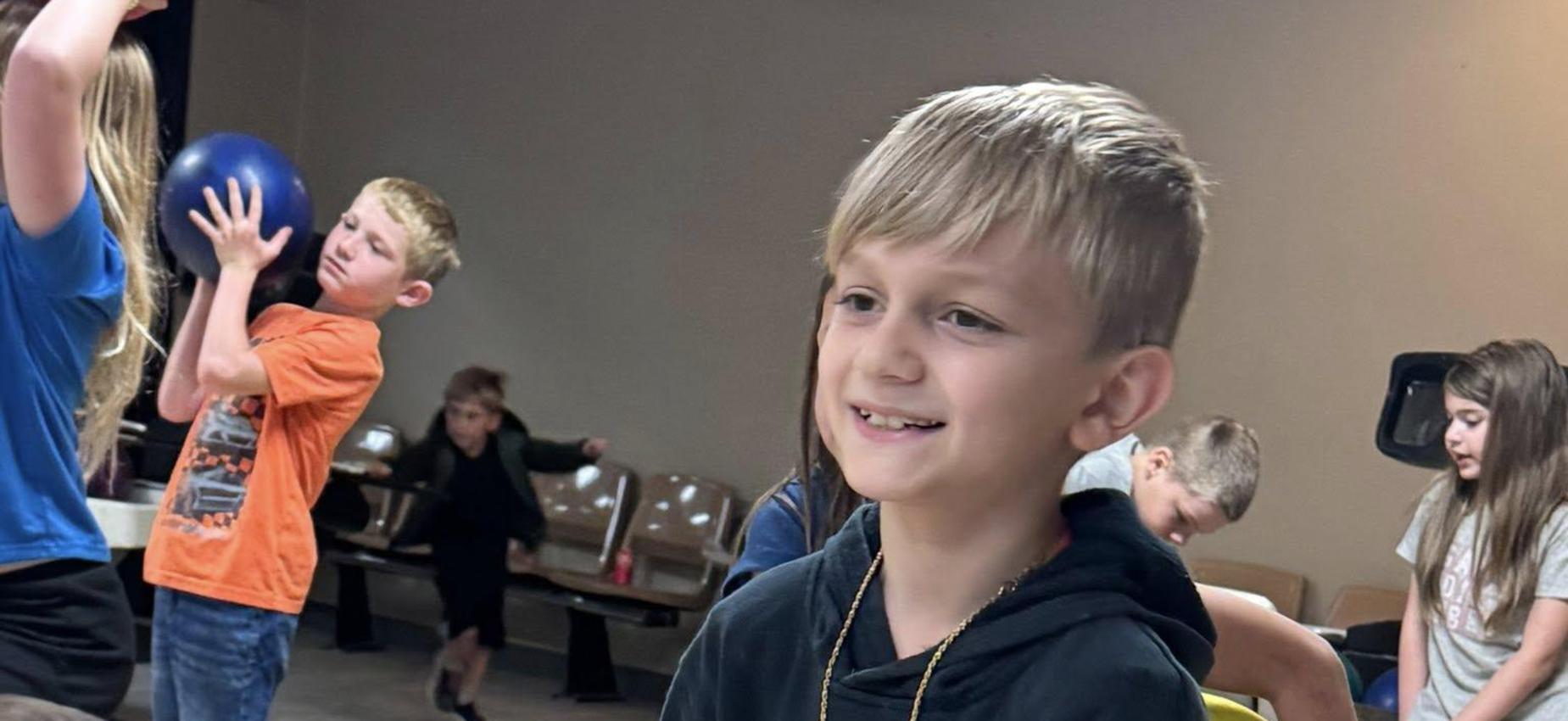 A group of children engaging in various activities indoors, with one boy smiling in the foreground.