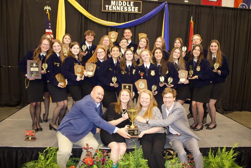 Smiling students and adults in professional attire with trophy for agricultural accomplishments