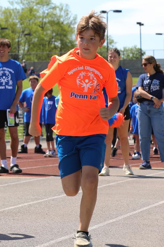 A Penn Yan student-athlete in an orange Special Olympics shirt runs on the track.