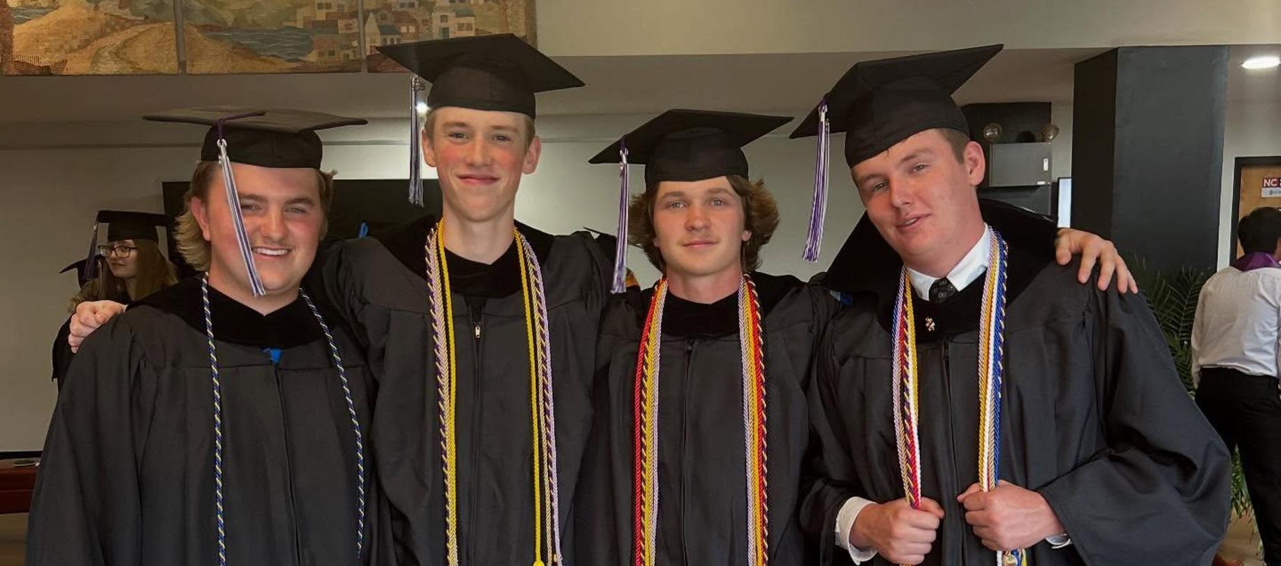 Four graduates in caps and gowns posing together, smiling at a celebration.