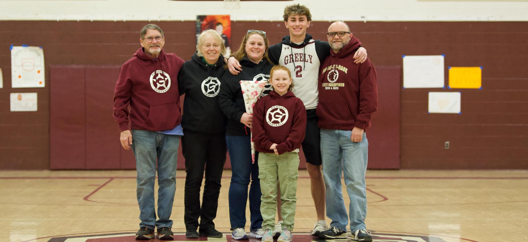 Six people pose together on a basketball court, smiling with a bouquet.