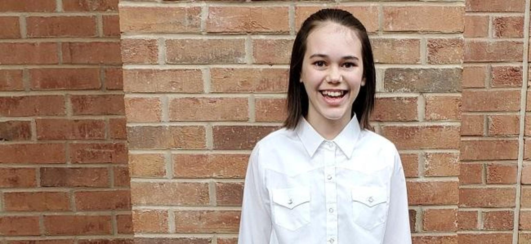 A student stands in front of a brick wall.