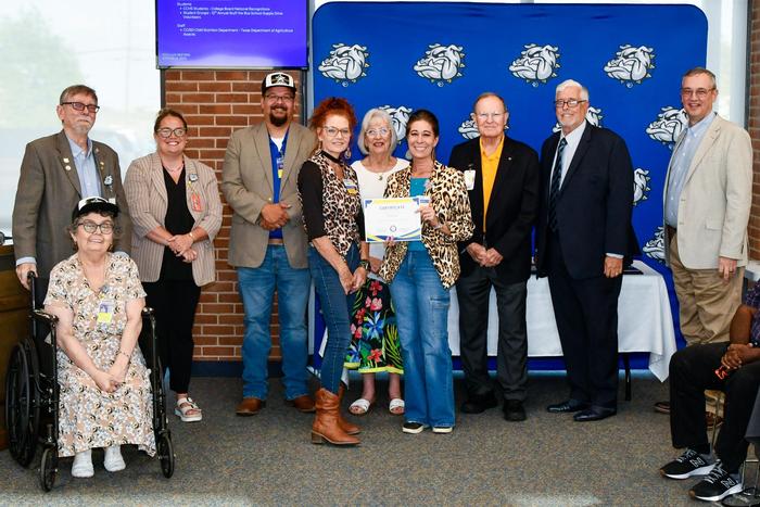 Two women holding an award and smiling with school board members