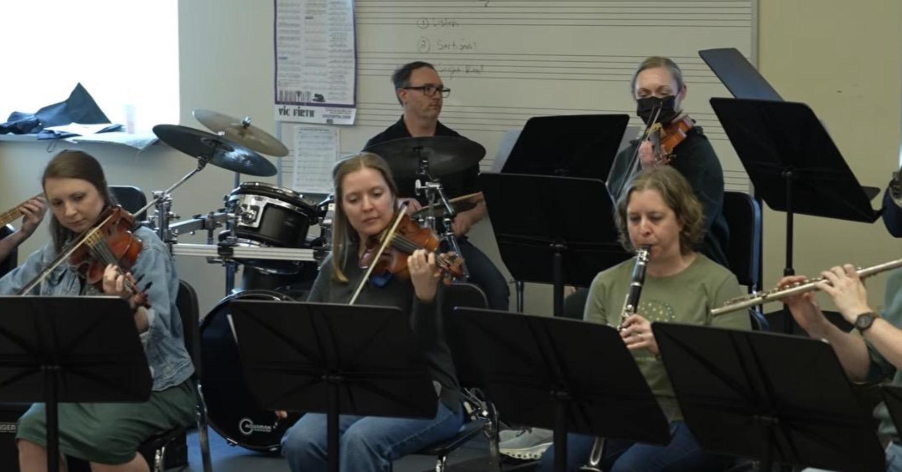 Musicians playing various instruments in a rehearsal setting.