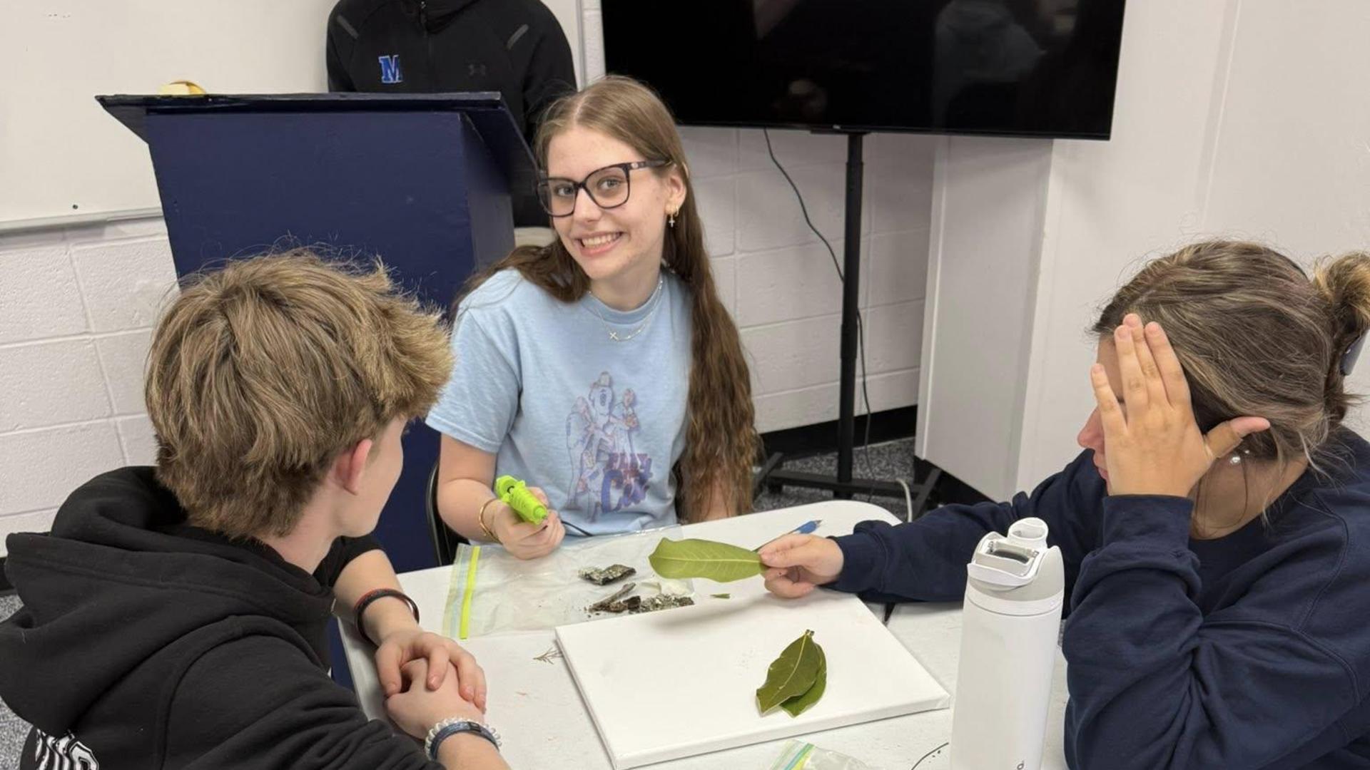Students work together on a project involving leaves and various materials.