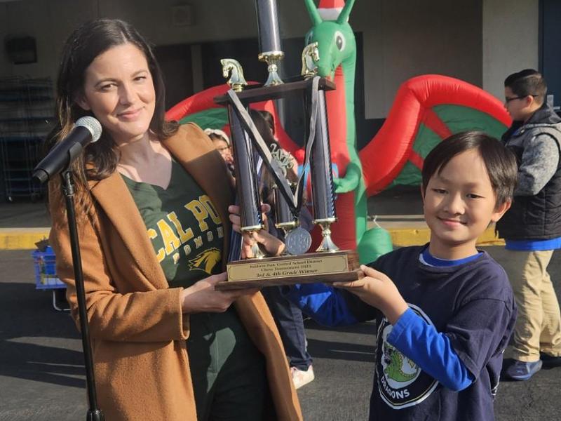 A woman presents a trophy to a young boy at an outdoor event.