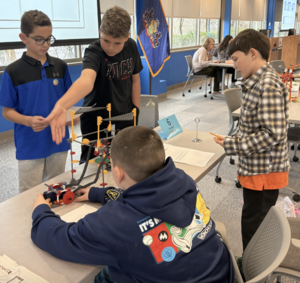 Four male students demonstrate their K'Nex prototype at the STEM Design Challenge.
