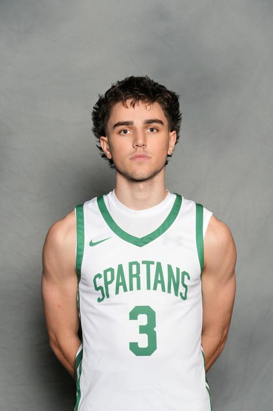 athlete standing with arms behind back in basketball uniform with grey backdrop