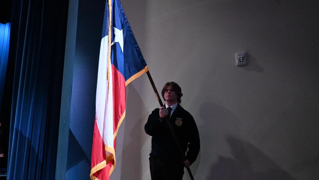 Boy in blue sweater holding a Texas flag on stage.