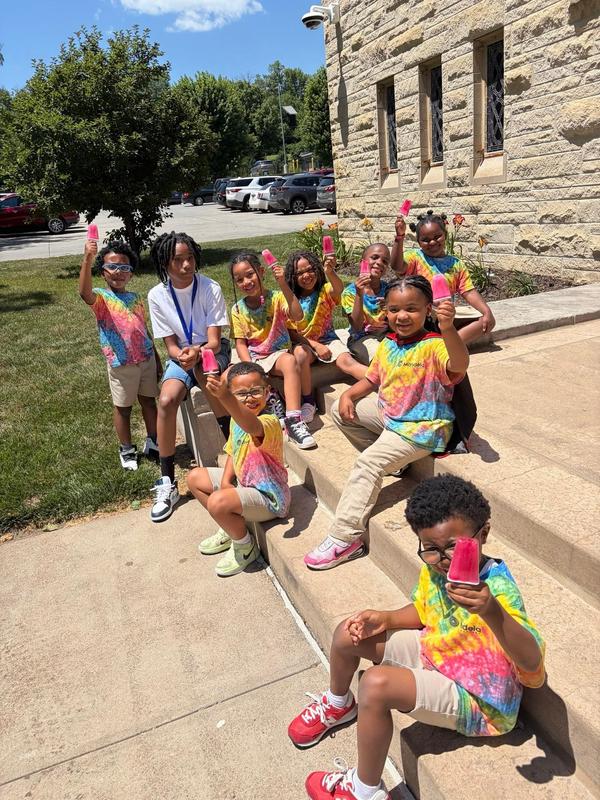 Scholars sit outside the front steps of the school eating popsicles
