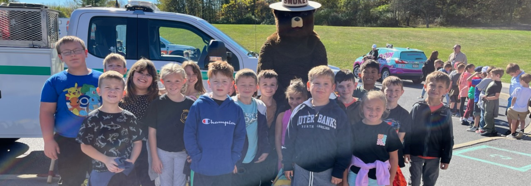 A group photo of children with a park ranger mascot and a police vehicle.