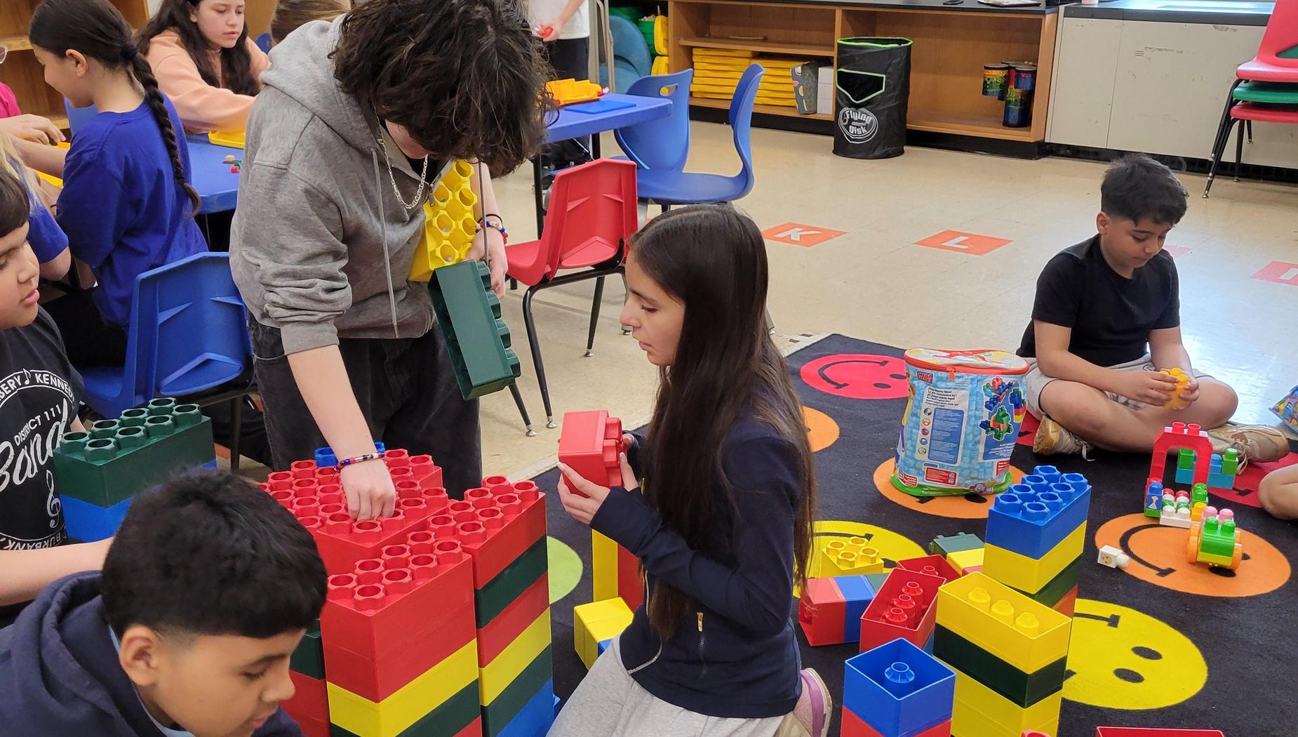 Kids stacking large colorful building blocks while others create structures nearby.