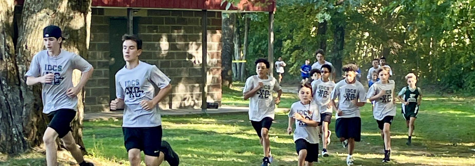 Group of boys running on a dirt path in athletic gear during a practice session.