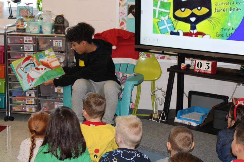 high schooler holding pete the cat book in front of kindergarten class