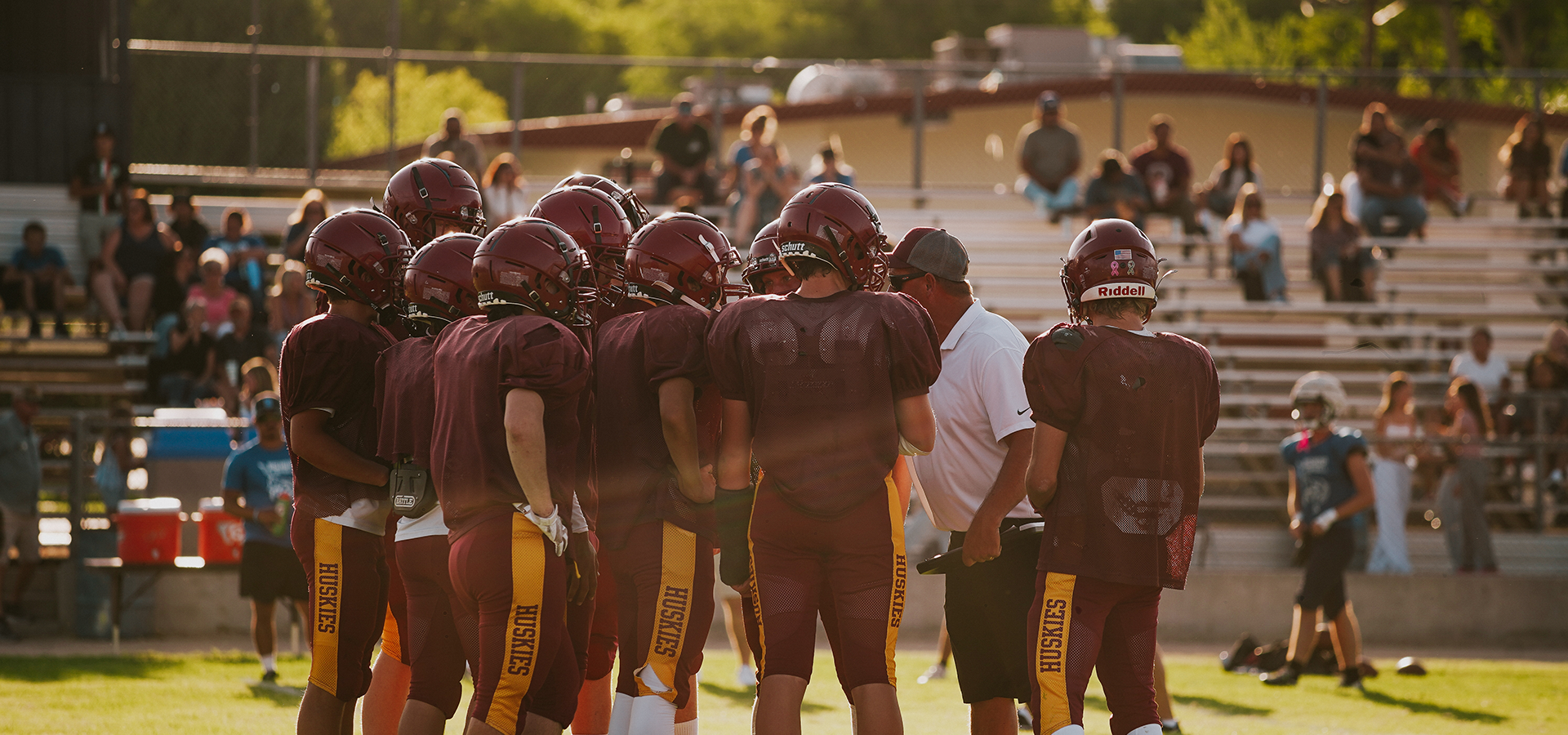 A football team in maroon uniforms huddled together on the field during a game.