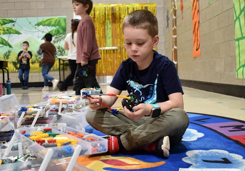 A child sitting on the floor plays with toys amid a colorful classroom setting.