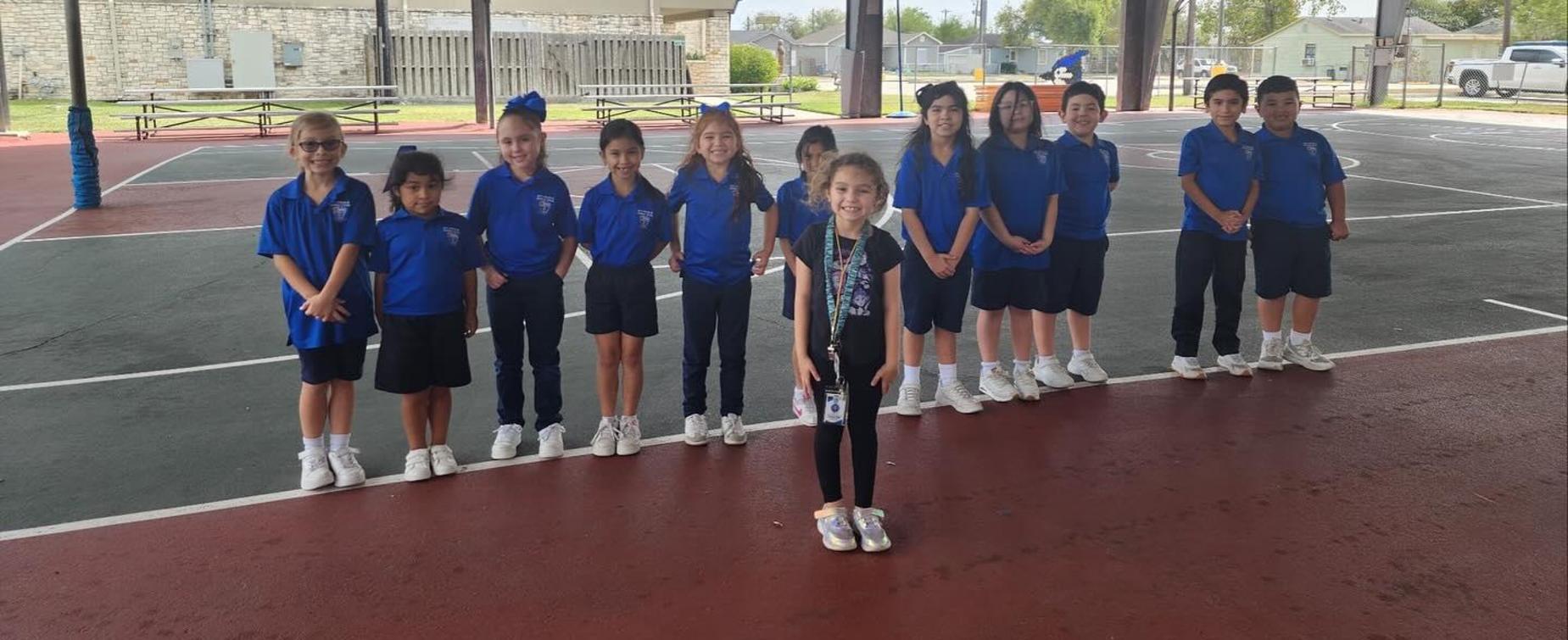 Group of children in blue uniforms posing together on a basketball court.