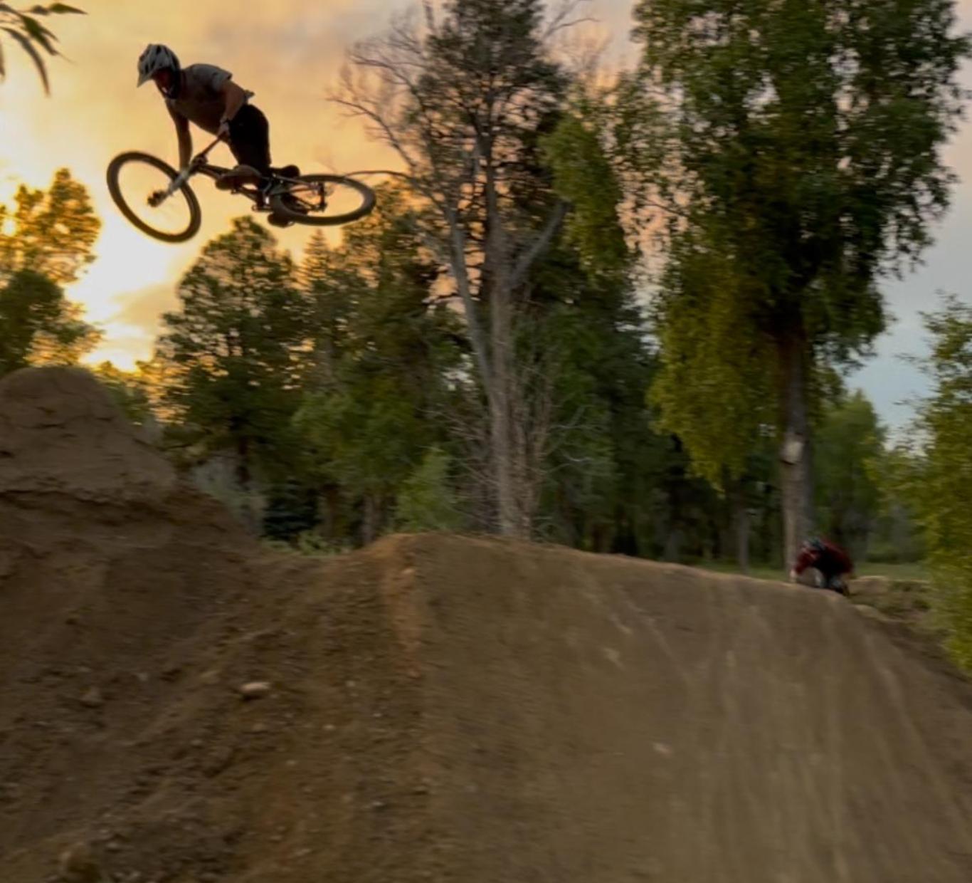 A cyclist performing a jump off a dirt ramp at sunset.