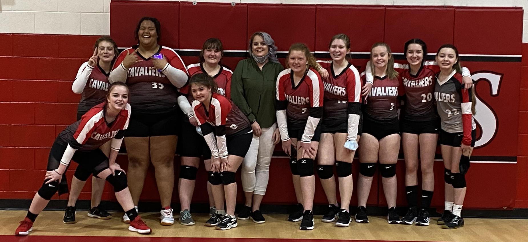 A group of volleyball players stand with their coach in a gym.