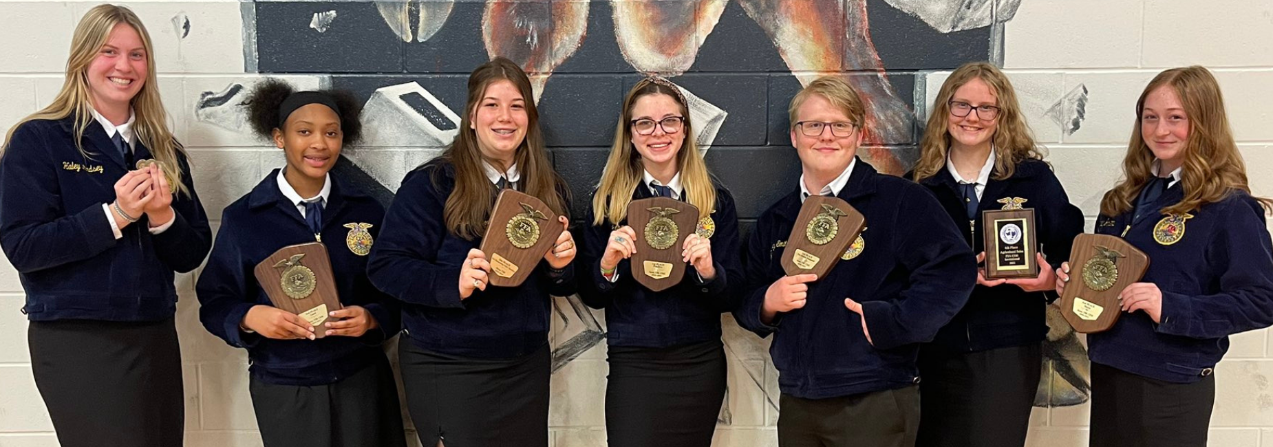 7 teen girls in matching FFA jackets holding awards they won