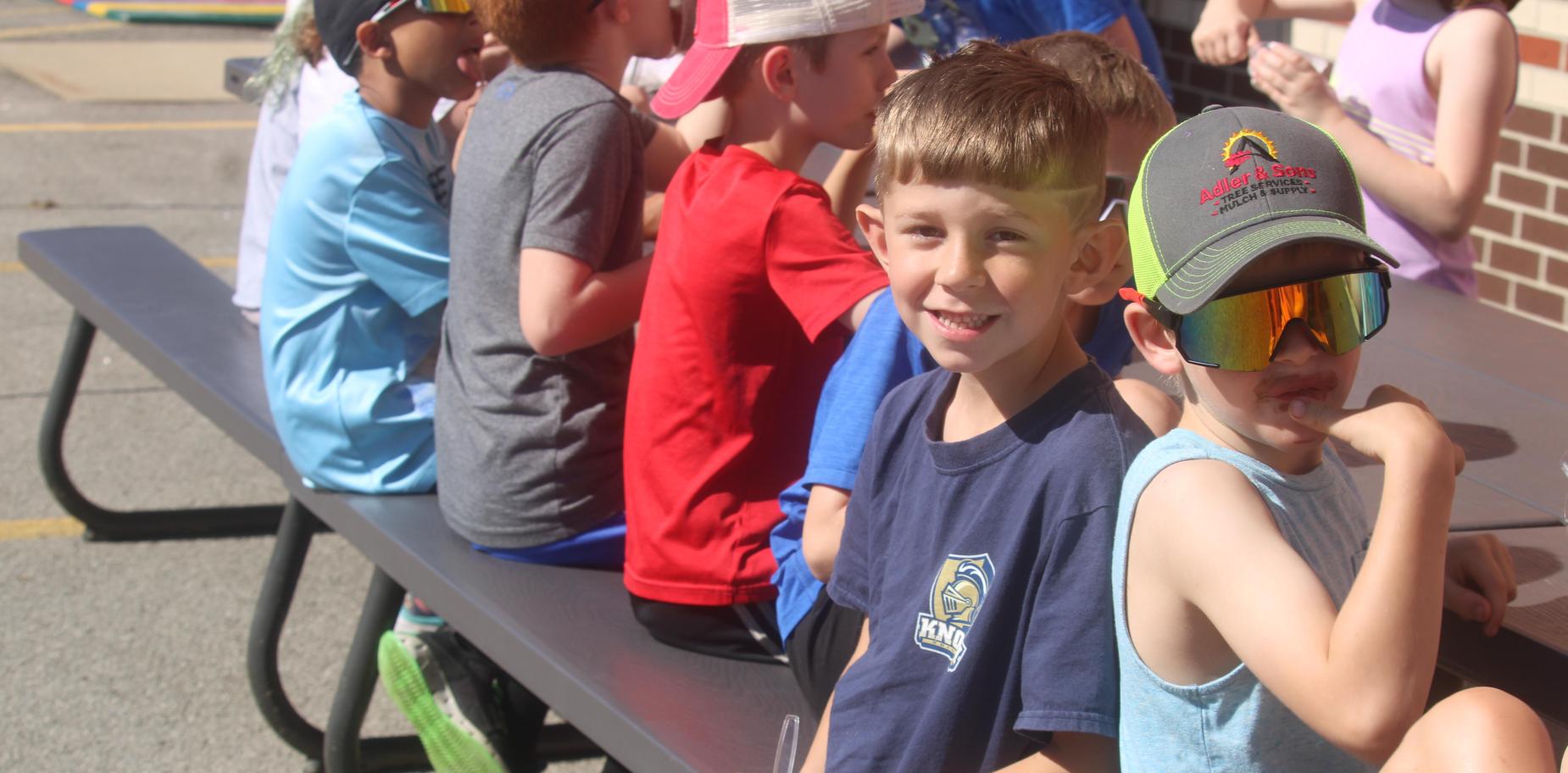 Two boys sitting at a table with snacks during an outdoor event.