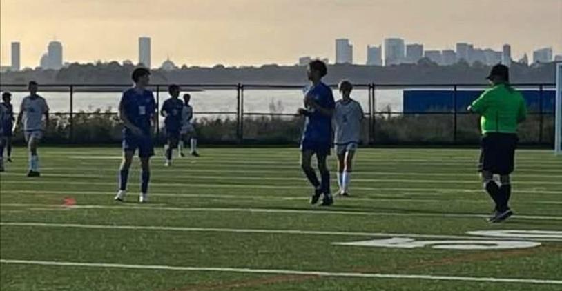 Soccer players on a field with a referee and a city skyline in the background.