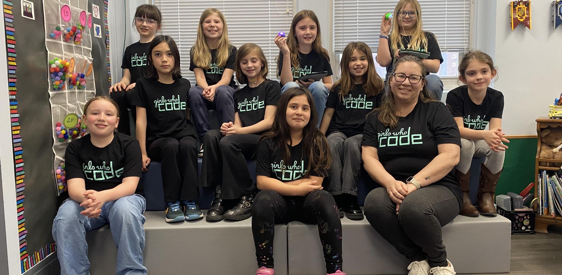 Group of girls wearing matching shirts, posing together in a classroom setting.