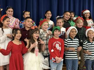 students standing on stage singing, wearing Christmas colors, doing hand motions