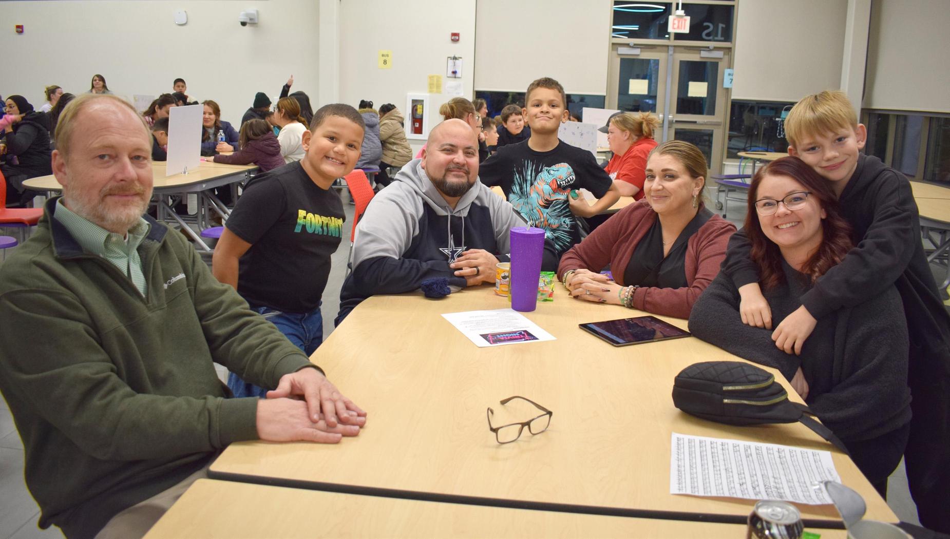 A group of adults and children gathered around a table, smiling and interacting.