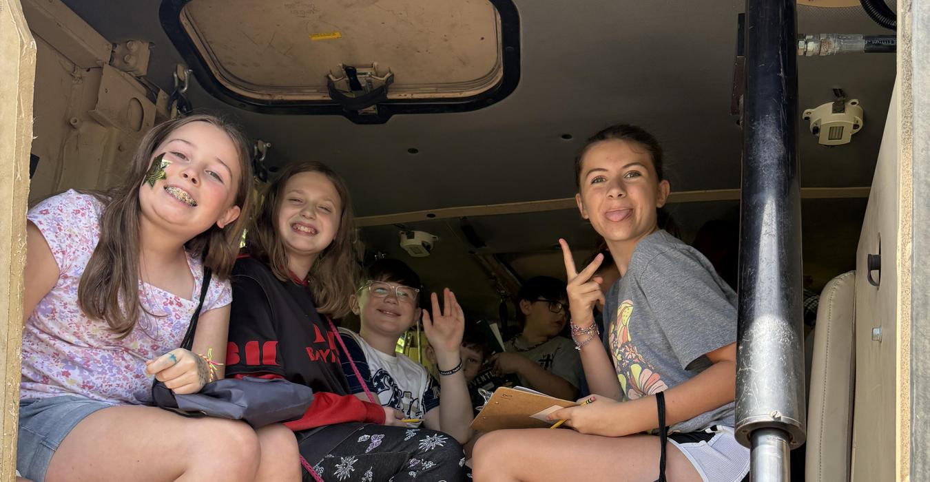 Group of smiling children sitting inside a vehicle, waving and posing.
